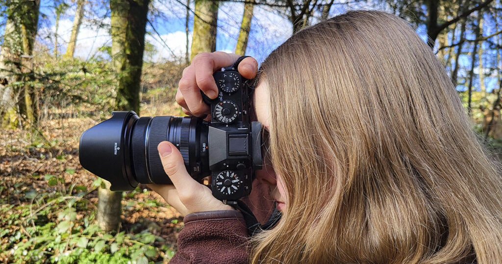 Person fotografiert mit Fujifilm-Kamera im sonnigen Wald.