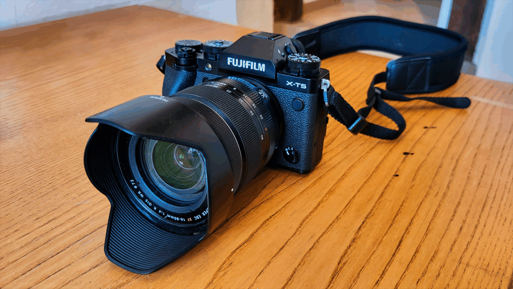 Fujifilm X-T5 Kamera mit Objektiv und Gurt auf einem Holztisch.