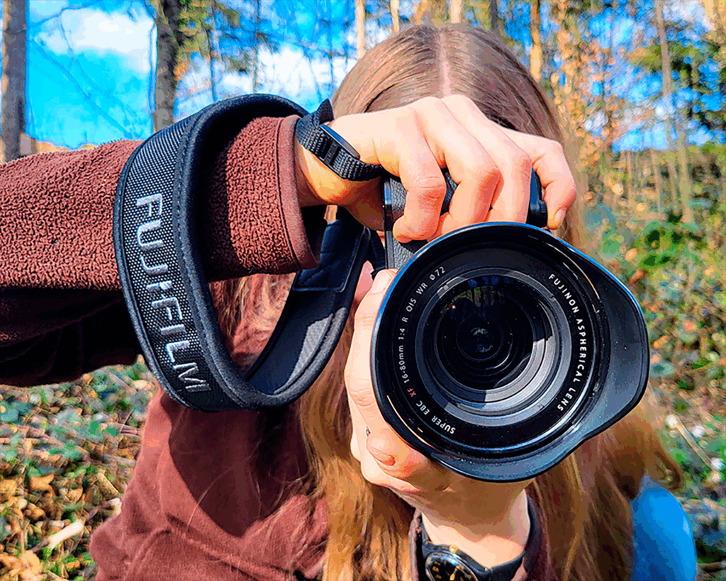 Person im Wald hält eine Fujifilm-Kamera direkt vor das Objektiv.
